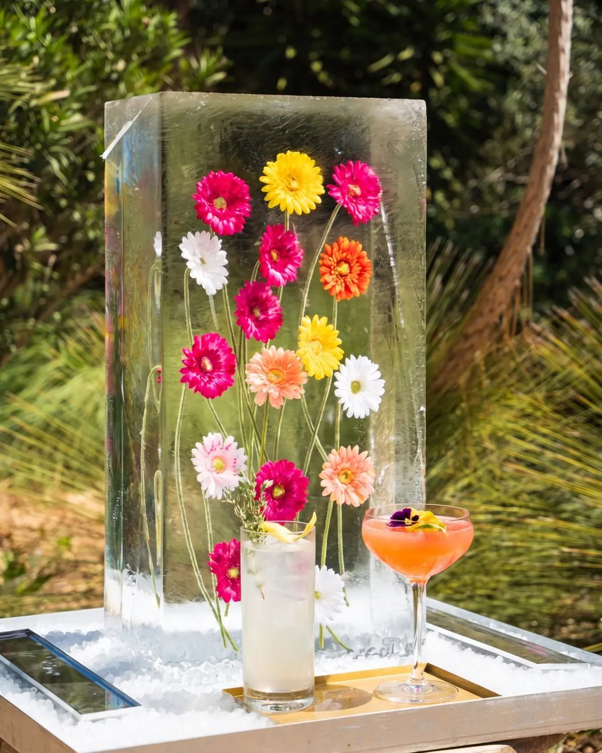 Block of ice with frozen coloured flowers and Green Jar signature cocktails served at its base, at an outdoor Ibiza event.